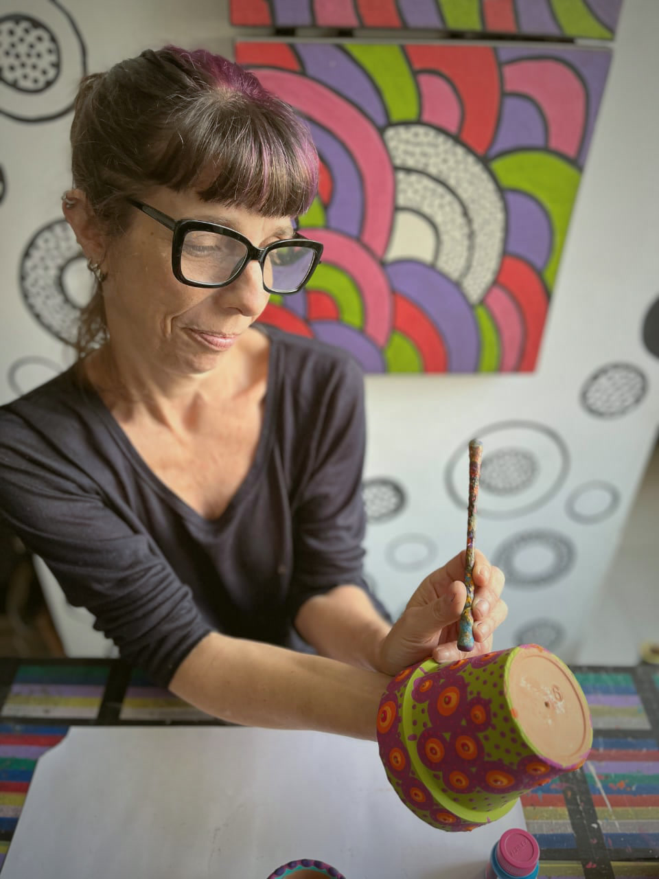 Dani Najman pintando pontos coloridos em um vaso de cerâmica no ateliê